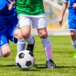 Beine von drei Fußballern im Trikot mit Ball