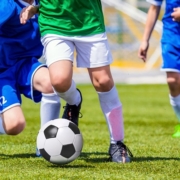 Beine von drei Fußballern im Trikot mit Ball