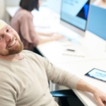 Fröhlicher Mann im Büro mit Be-Happy Notiz am Kopf