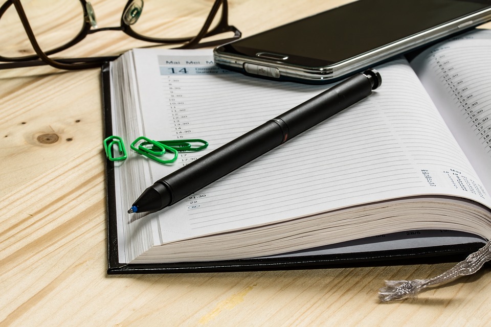 Kalenderbuch, Stift, Handy und Brille liegen auf einem Tisch